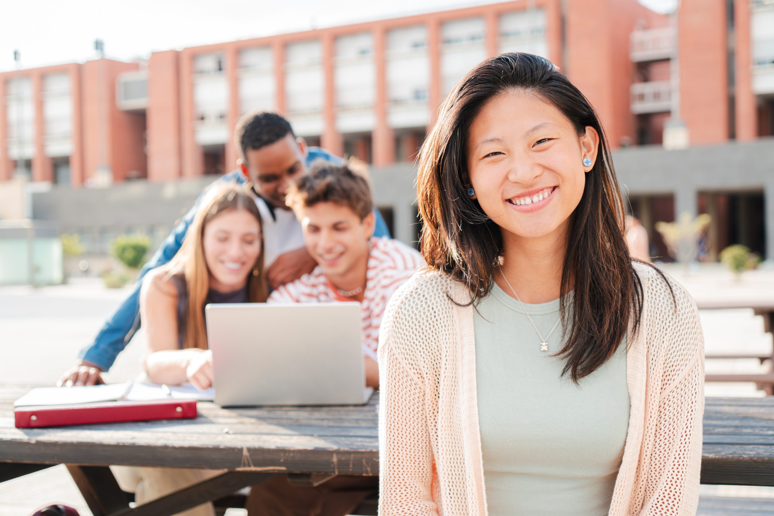 On foreground an asian schoolgirl staring front behind her multiracial friends. Young chinese teenage female student, smiling and looking at camera sitting with her classmates at university campus. High quality photo
